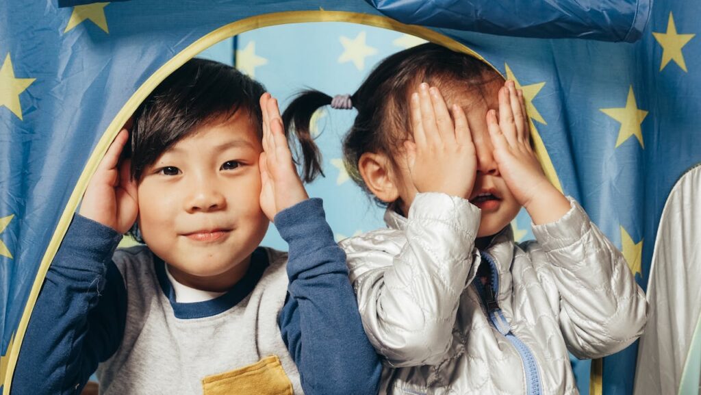 Two kids playfully engage in peek-a-boo inside a star-themed tent.